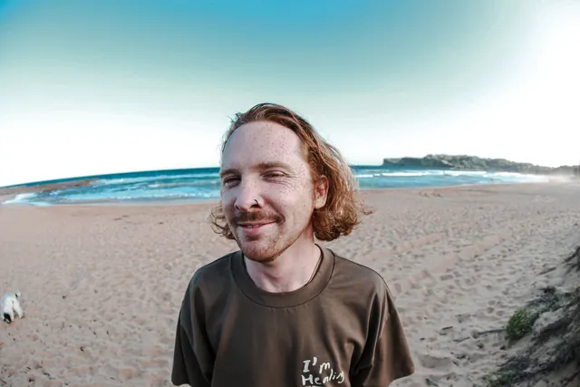 Ben smiling on the beach, with the ocean behind him.