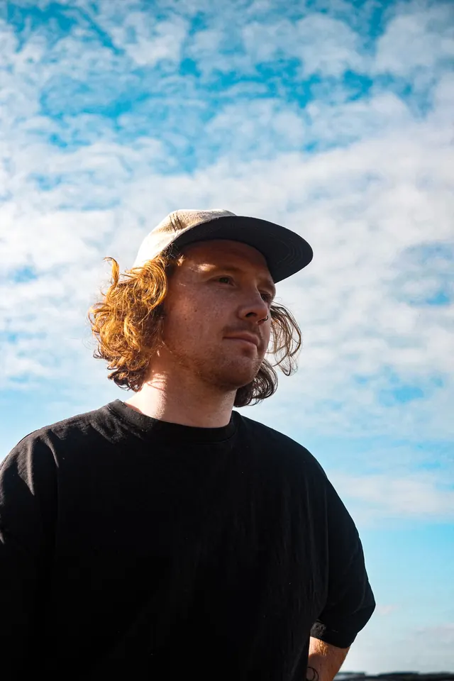 A portrait of Ben in a cap beneath a blue, cloud-filled sky.