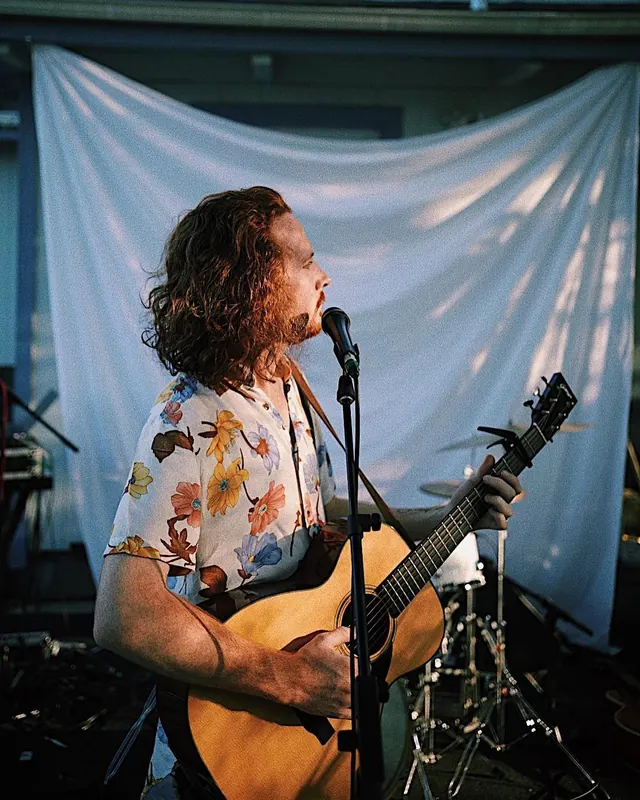 A film photograph of Ben singing with an acoustic guitar.
