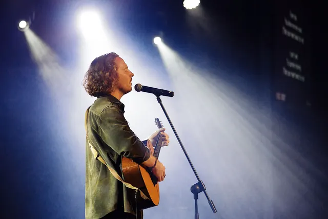 Ben singing and playing acoustic guitar beneath the stage lights.