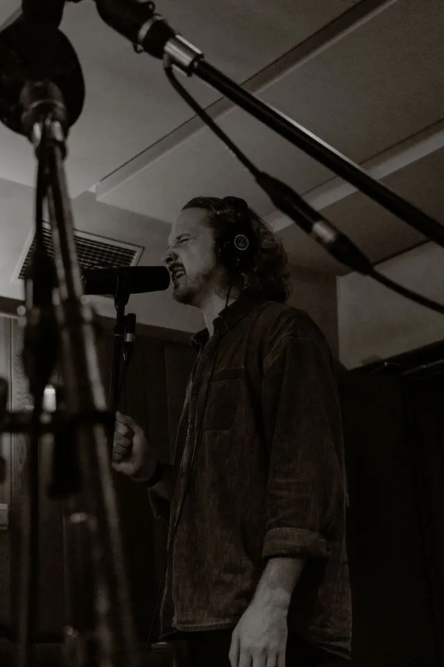 Ben recording vocals, wearing headphones beside a microphone.
