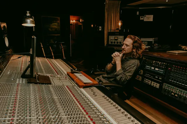 Ben sitting at the mixing desk in a warmly lit recording studio.